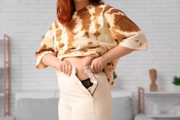 Image of woman trying to do her trousers up after pregnancy weight gain Wiltshire