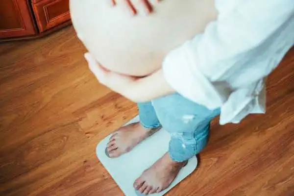 Image of woman weighing herself and experiencing weight gain through pregnancy Wiltshire